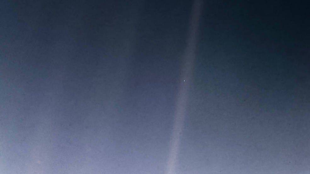 The Pale Blue Dot: Earth appears as a single bright pixel inside a band of scattered sunlight, photographed by the Voyager 1 spacecraft from about six billion kilometres away
